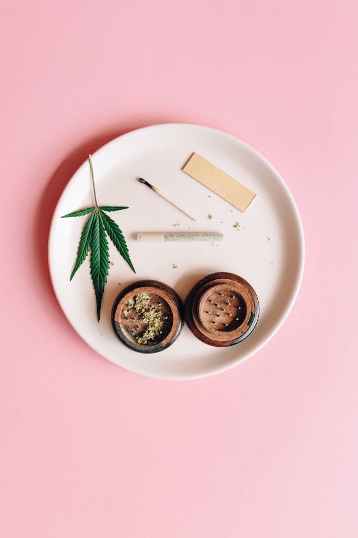 Services A cannabis leaf, grinder, and joint on a pink background, symbolizing relaxation.